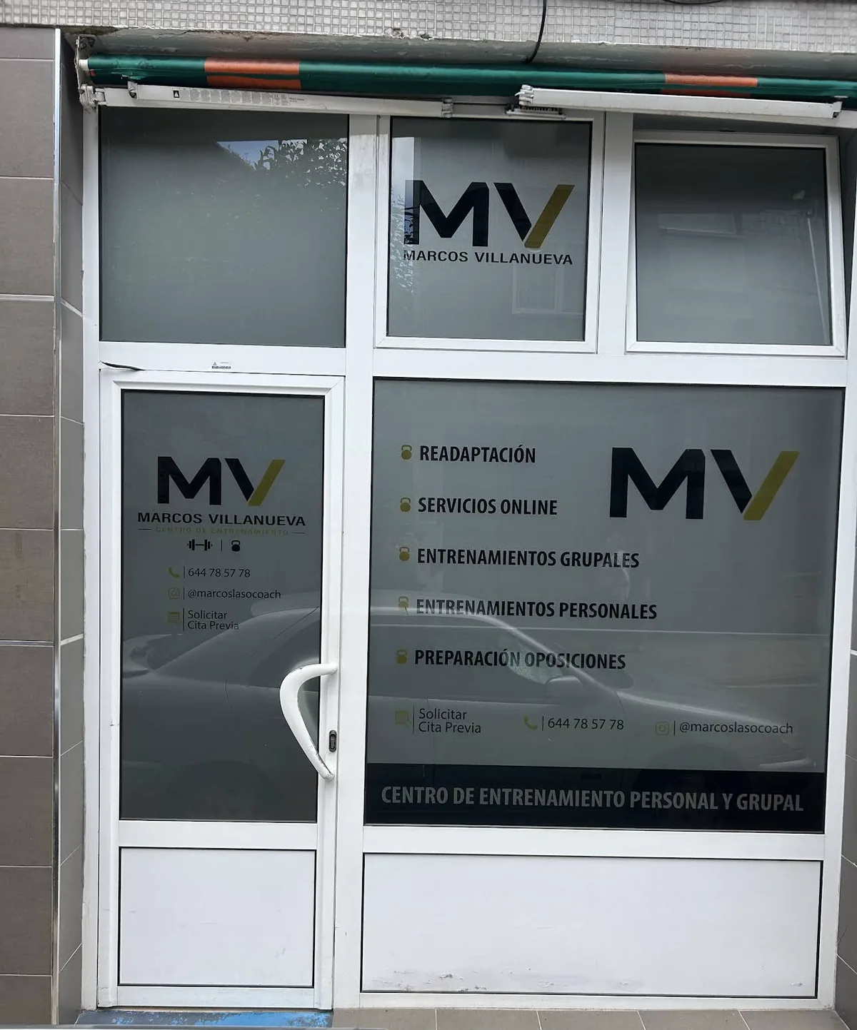 Fachada del centro en Candás con el logo MV y la lista de servicios en el cristal