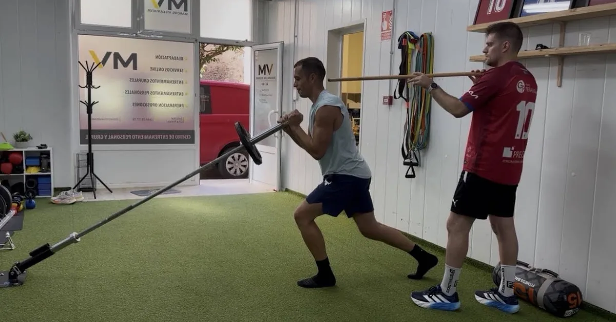 Entrenamiento de zancada con barra anclada y compañero con pica, junto a la entrada del centro